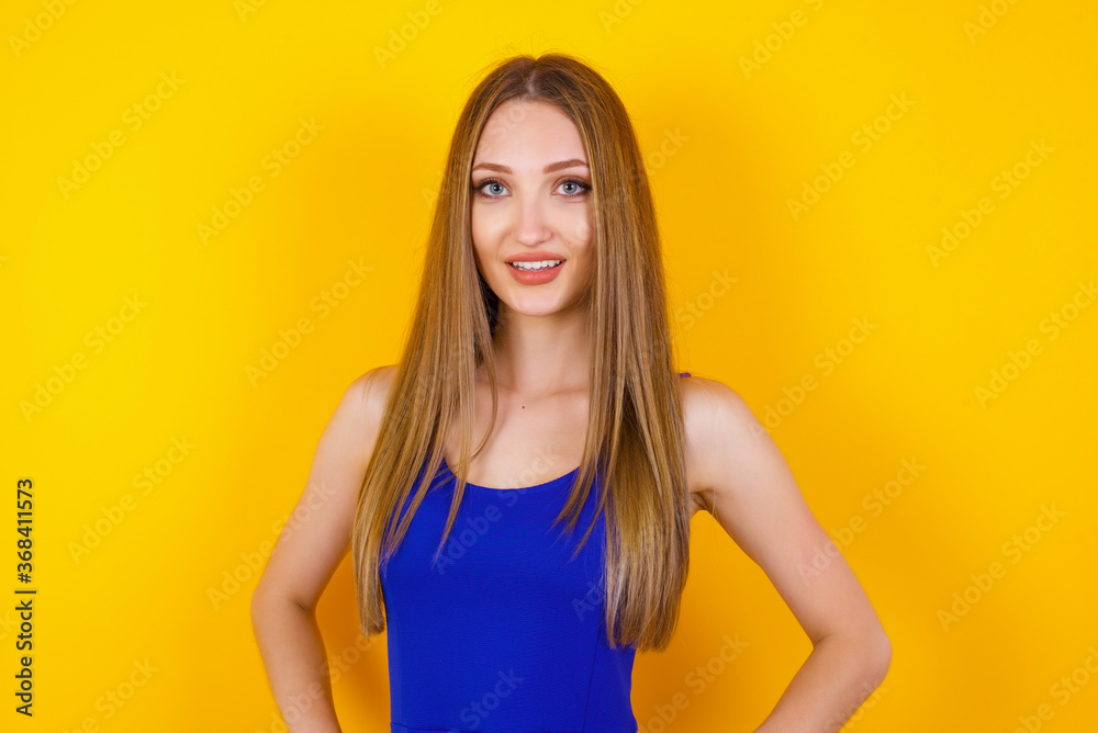 Confidence and business concept. Portrait of charming successful young girl, smiling broadly with self-assured expression while holding hands in pockets standing against gray wall. Confidence and business concept. Portrait of charming successful young girl, smiling broadly with self-assured expression while holding hands in pockets standing against gray wall.