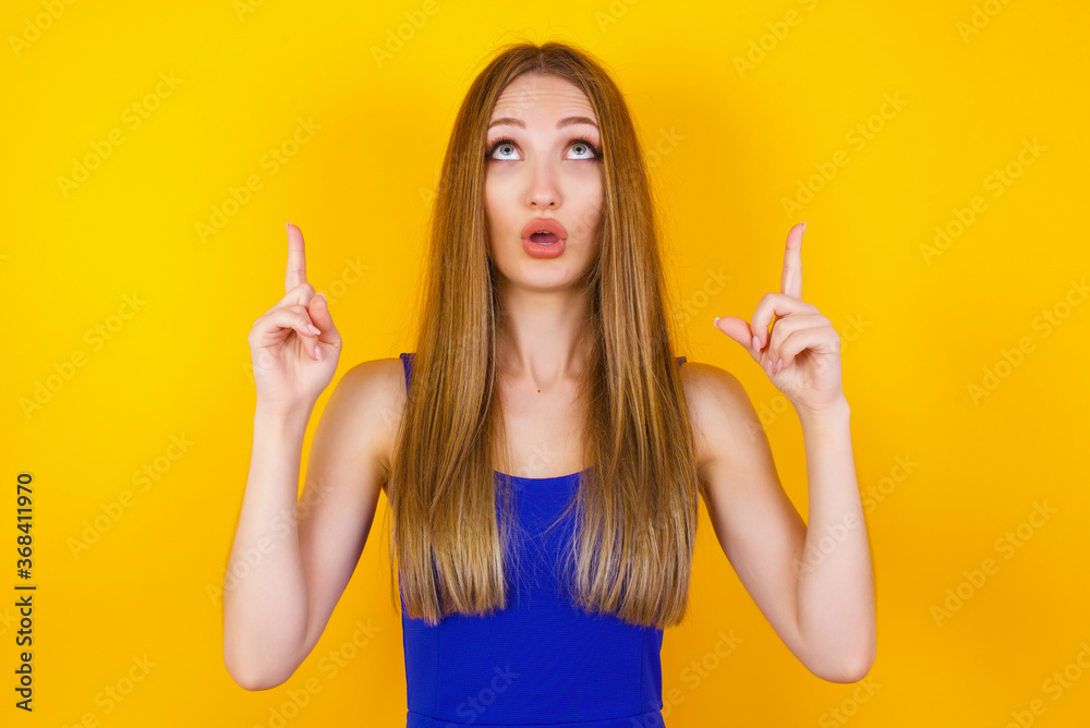 Portrait of beautiful elegant woman over isolated background being amazed and surprised looking and pointing up with fingers showing something strange. Portrait of beautiful elegant woman over isolated background being amazed and surprised looking and pointing up with fingers showing something strange.