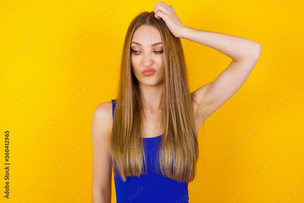 Oops, what did I do? Beautiful blonde woman holding hand on head with frightened and regret expression. Wearing casual clothes standing against gray background.