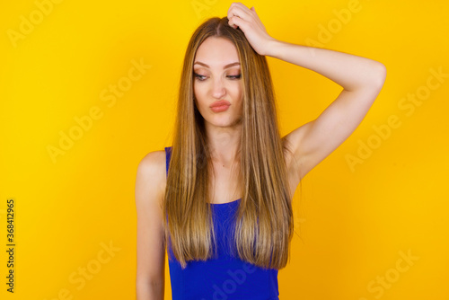 Oops, what did I do? Beautiful blonde woman holding hand on head with frightened and regret expression. Wearing casual clothes standing against gray background. © Jihan