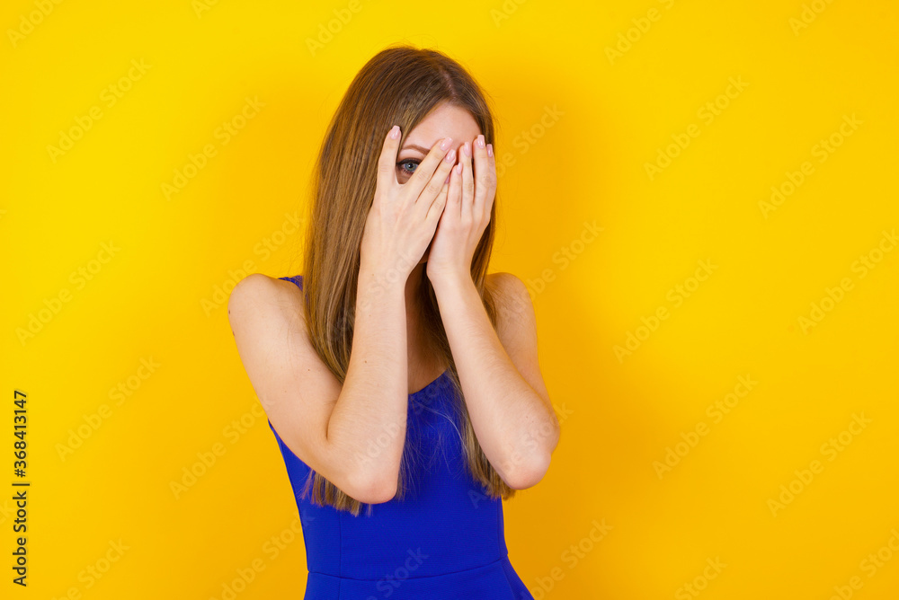Anxiety - a conceptual image of a beautiful young caucasian woman covering her face with her hands and peering out with one eye between her fingers standing indoors. Scared from something or someone. Anxiety - a conceptual image of a beautiful young caucasian woman covering her face with her hands and peering out with one eye between her fingers standing indoors. Scared from something or someone.