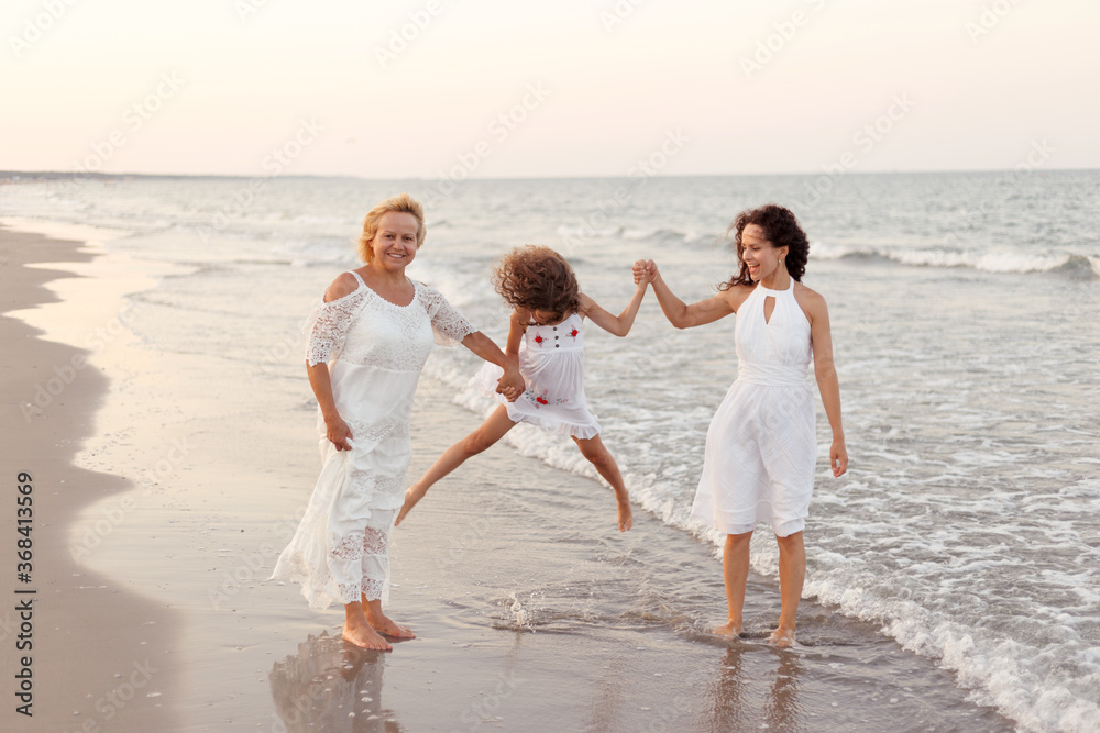 Portrait of three generations of women standing at beach holding hands.