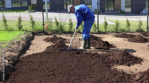 Skilled worker man with rake tool leveling fertile soil compost for lawn sowing