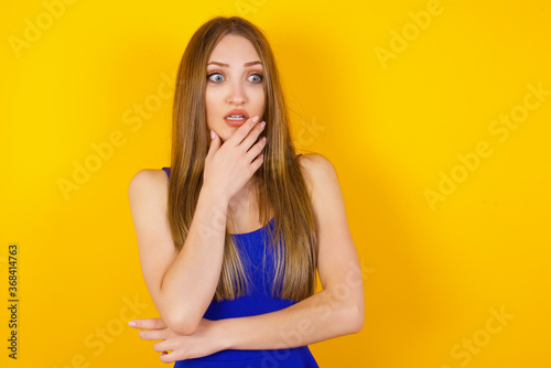 Anxiety - a conceptual image of a beautiful young caucasian woman covering her mouth with her hands and standing indoors. Scared from something or someone bitting nails