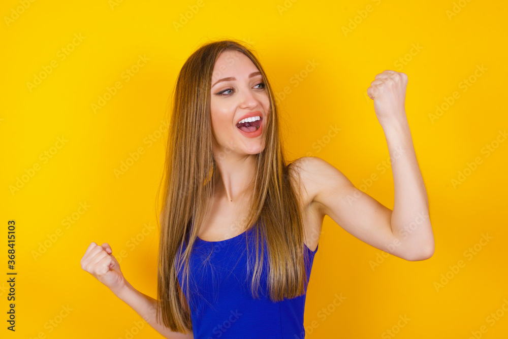 Attractive young caucasian woman celebrating a victory punching the air with her fists and a beaming toothy smile over a white studio background with copy space. Attractive young caucasian woman celebrating a victory punching the air with her fists and a beaming toothy smile over a white studio background with copy space.