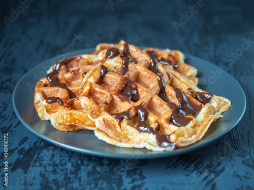 Cottage cheese waffles with chocolate topping on a dark plate on a gray background