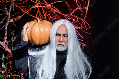 Happy Halloween. Evil wizard hold orange pumpkin. Mature man magician in witch hat. Traditional food. Fantasy horror Halloween. Halloween banner. Devil vampire man. Handsome Demon with Jack o lantern.