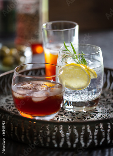 Glasses of brandy, gin & tonic and vermouth on drinks tray. Olives and bottle in background.