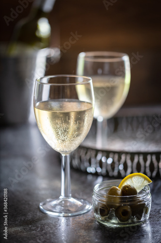 2 glasses of chilled white wine with bowl of olives.  Drinks tray and wine bucket in background
