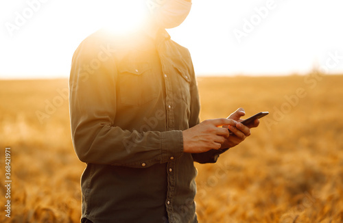 Farmer in sterile medical masks with phone in their hands in a wheat field during pandemic. Agro business. Harvesting. Covid-2019.
