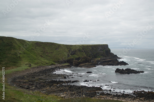 Rocky formations on the coast of Northern Ireland. Tall grassy cliffs are hit by several waves