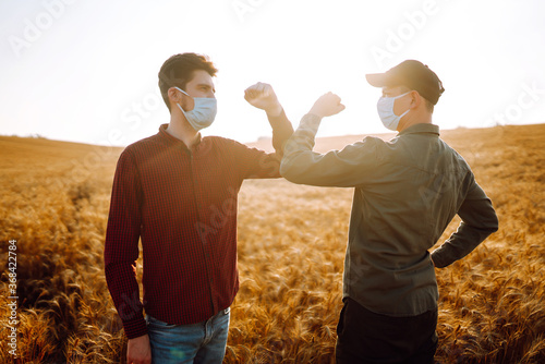Two farmers in sterile medical masks greet their elbows on a wheat field during pandemic. Stop handshakes. Covid-2019.