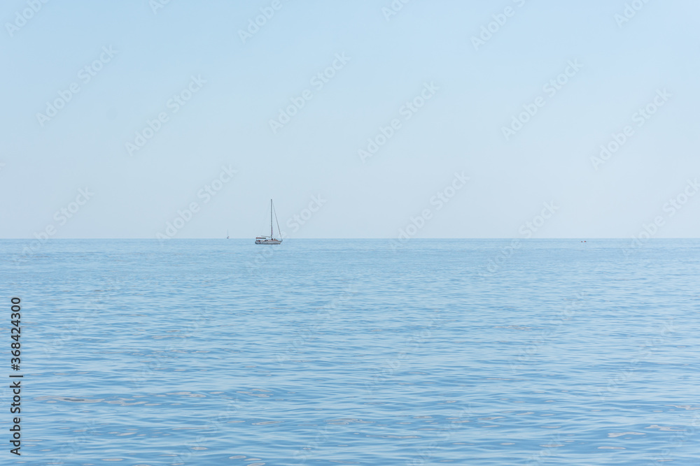 A lone sailboat against the blue sea and sky. The tranquil sea. Light blue sea background. Summer vacation on the deck of a small yacht. Relaxation and calm.