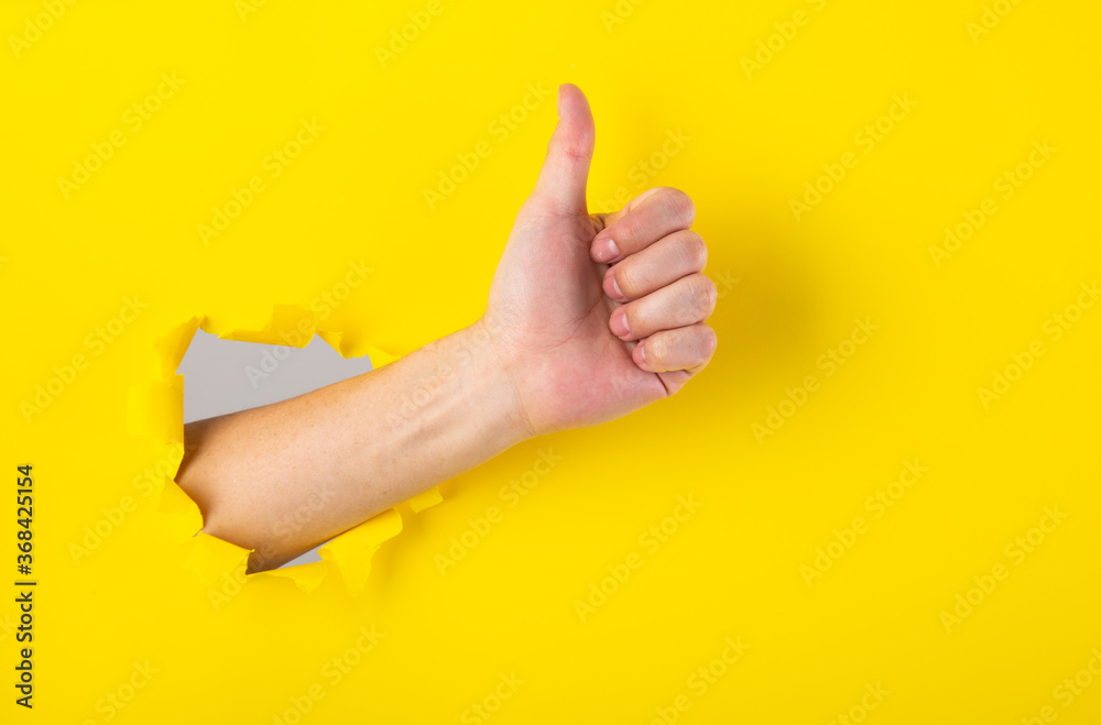 Hand showing a thumb up sign through a ripped hole