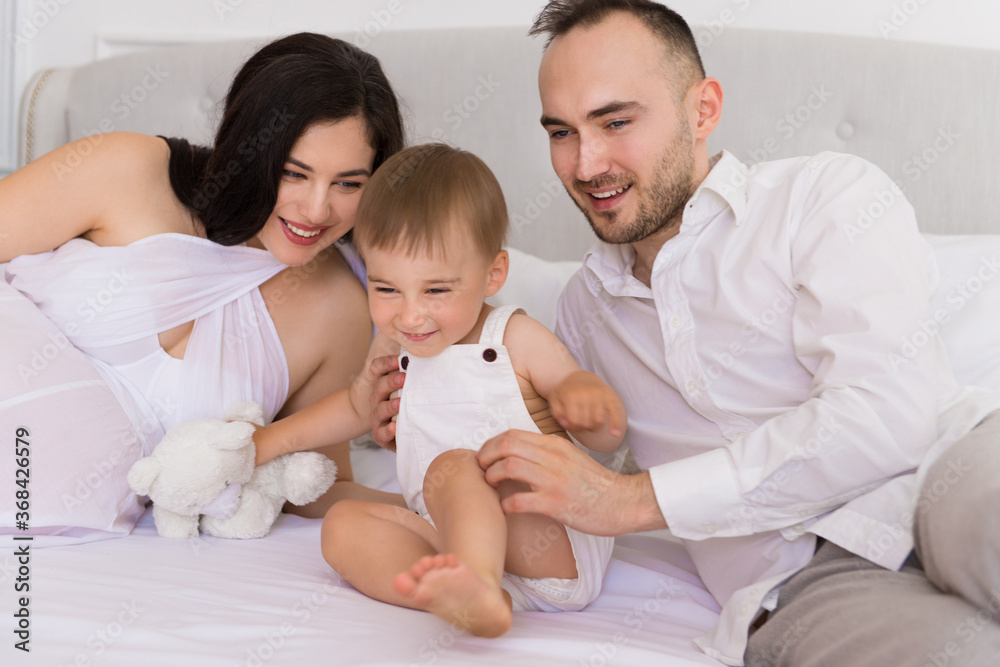 happy family on bed in bedroom married couple with small child and pregnant woman happy family on bed in bedroom married couple with small child and pregnant woman