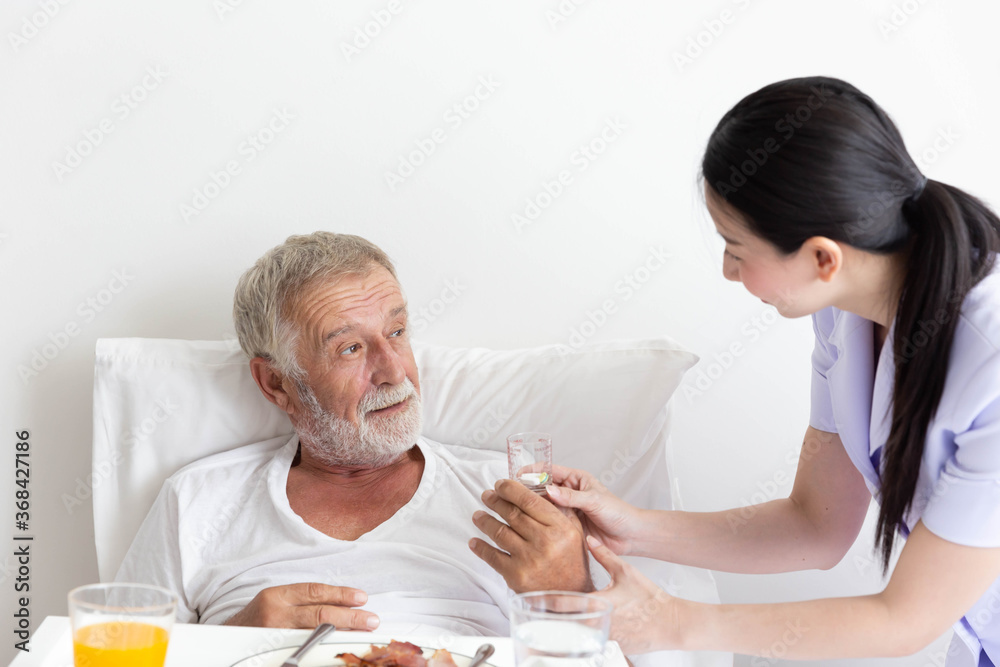 Nurse give medicine pills to elderly senior patient while he is in his bed with breakfast Nurse give medicine pills to elderly senior patient while he is in his bed with breakfast