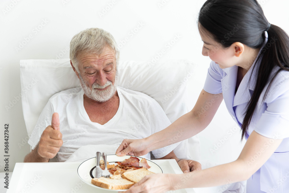 Young female nurse take care a senior retirement male serving breakfast on bed and old man love it Young female nurse take care a senior retirement male serving breakfast on bed and old man love it