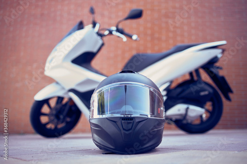 Close-up of a motorcycle black helmet with a white motorcycle in the background. Front View