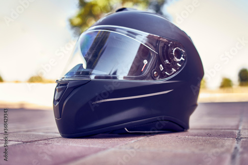 Close-up of a black helmet on the ground with the visor closed. Side view.