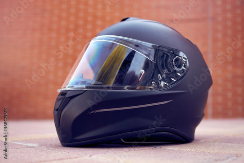 Close-up of a black helmet on the ground with the visor closed. Side view.