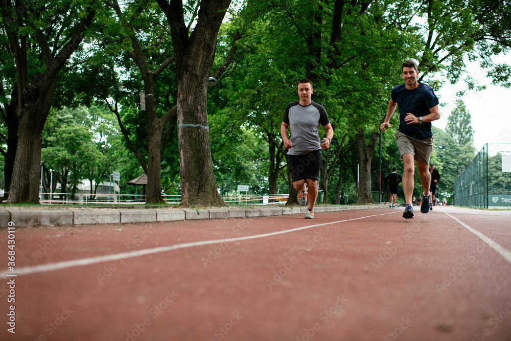 Young men training on a race track. Two young friends running on the athletics track Young men training on a race track. Two young friends running on the athletics track