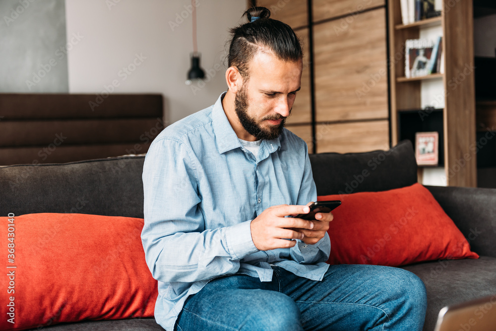 Smiling man sitting on sofa using cell phone.