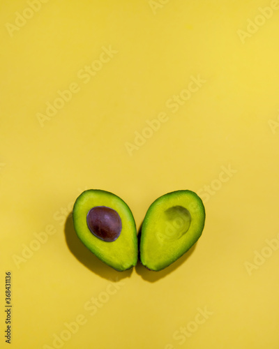 Avocado cut in half on yellow surface. Close-up of whole avocado cut in half isolated on yellow background.