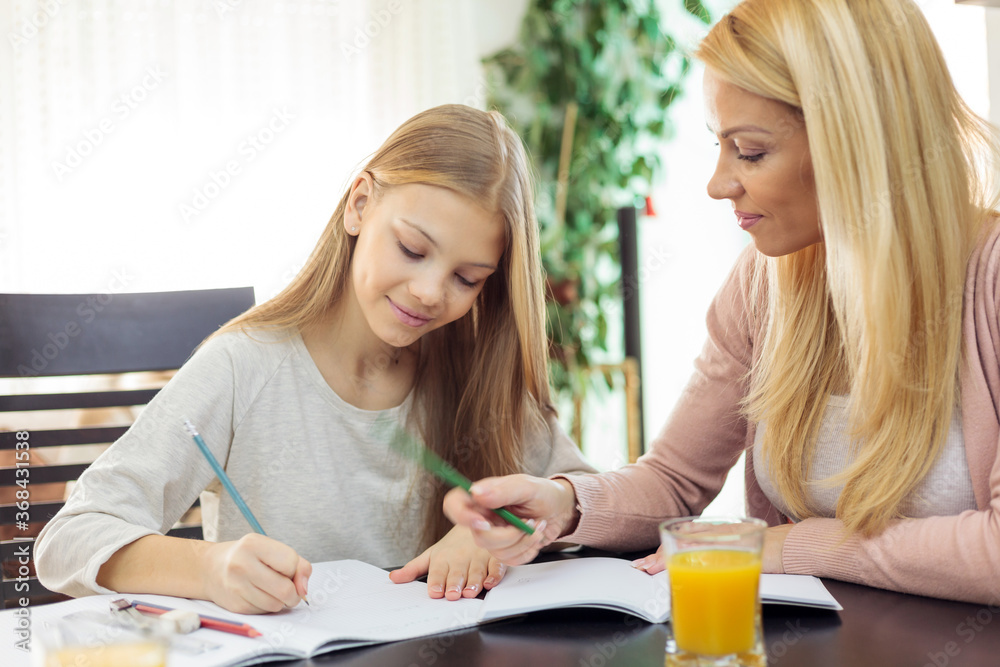 Happy young blond haired Caucasian woman helping her teenage daughter with homework and studying during pandemic lockdown Happy young blond haired Caucasian woman helping her teenage daughter with homework and studying during pandemic lockdown