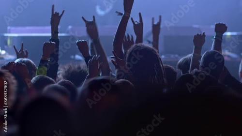 Unrecognizable fans dancing at a concert or festival party. Silhouettes of concert crowd in front of bright stage lights. slow motion photo