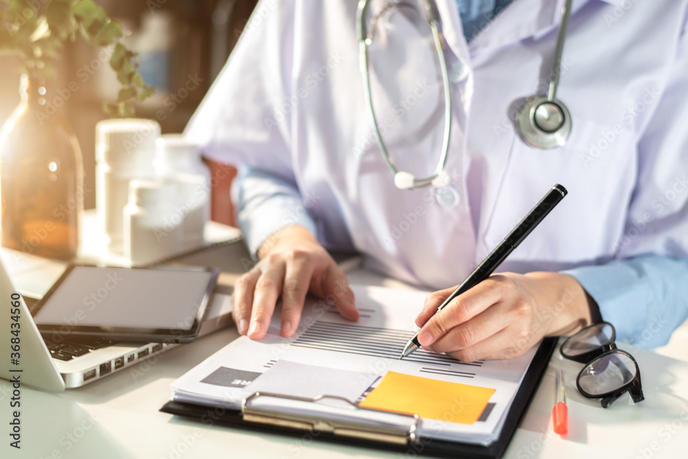 Female in uniform of doctor using digital technology laptop for Output Device and writing a patient report on the office desk. Female in uniform of doctor using digital technology laptop for Output Device and writing a patient report on the office desk.