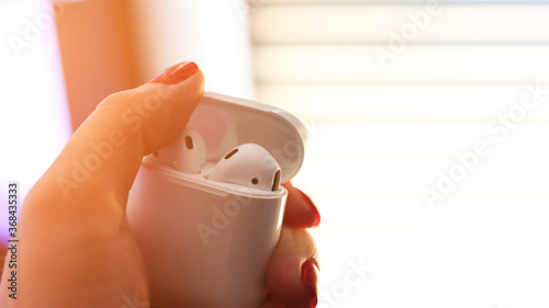 White case with wireless headphones in female hands. Close-up, sunlight. photo