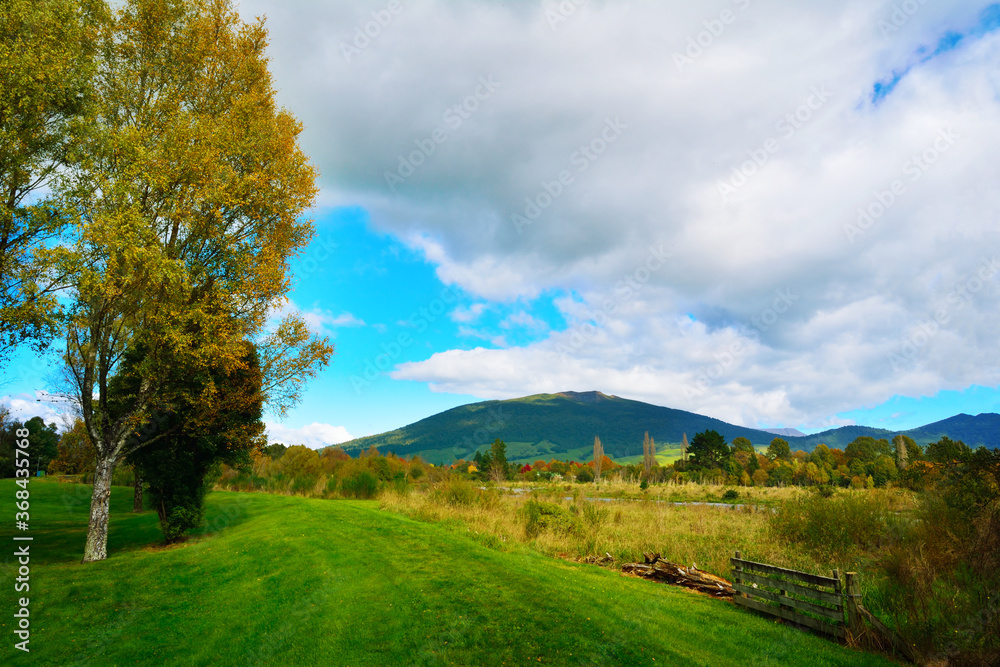 Grass footpath on the high bank of Tongariro river leading toward Turangi town and Tongariro National park. Autumn days at North Island, New Zealand Grass footpath on the high bank of Tongariro river leading toward Turangi town and Tongariro National park. Autumn days at North Island, New Zealand