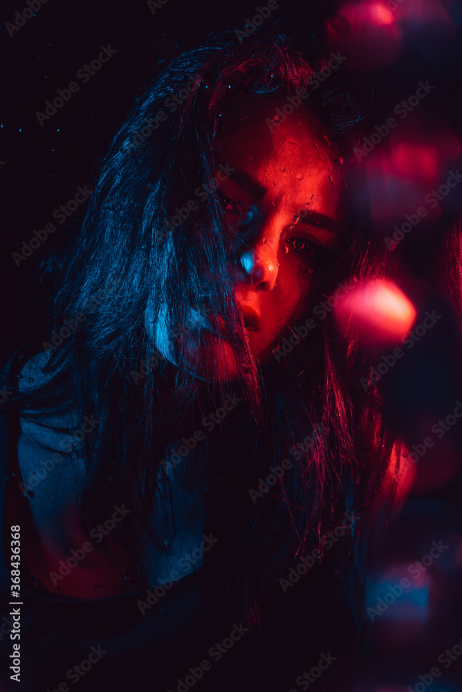 Sensual portrait of sad melancholic lonely girl behind glass with raindrops