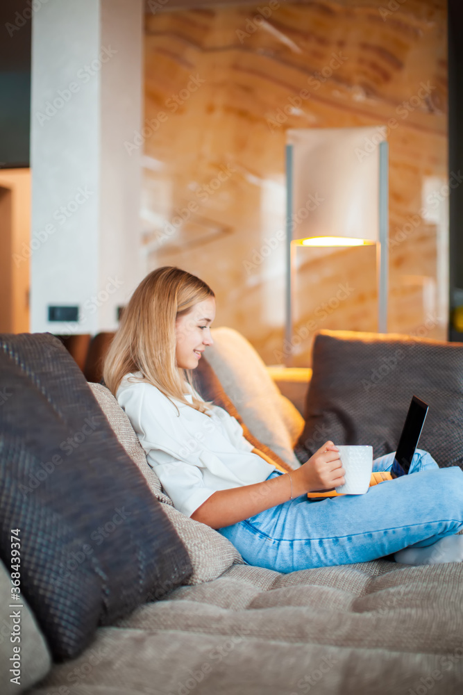 Pretty young teen girl sitting on sofa in Lotus position with laptop and cup of tea watching TV series. Cozy home photo Pretty young teen girl sitting on sofa in Lotus position with laptop and cup of tea watching TV series. Cozy home photo