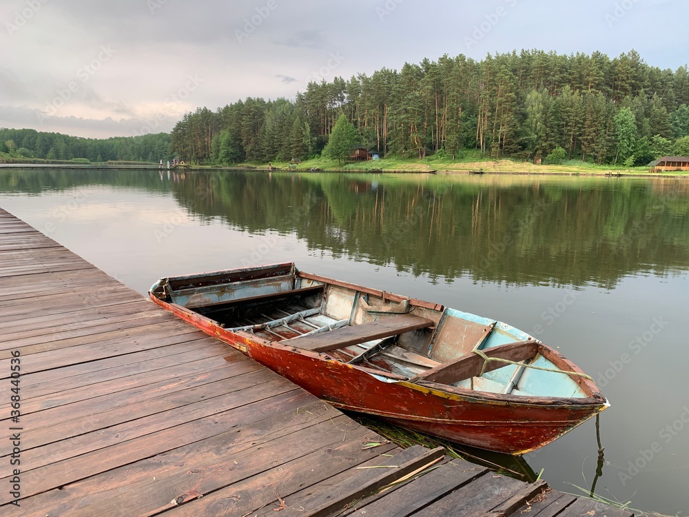 Wooden boat on the pier on the background of the lake. Fishing boat on the shore of a forest reservoir. The boat is tied to the shore. Concept: outdoor recreation, tranquility by the water.