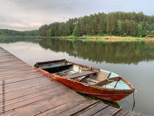 Wooden boat on the pier on the background of the lake. Fishing boat on the shore of a forest reservoir. The boat is tied to the shore. Concept: outdoor recreation, tranquility by the water.