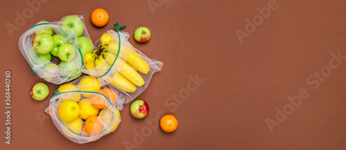 Wide banner Fresh ripe and juicy fruits in reusable eco friendly mesh bags on the brown background. Plastic free, zero waste, and sustainable living concept. Reusable using. Copy space. Top view.
