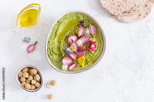 Colorful green hummus bowl with baked radish and edible flowers, vegetarian meal, top view