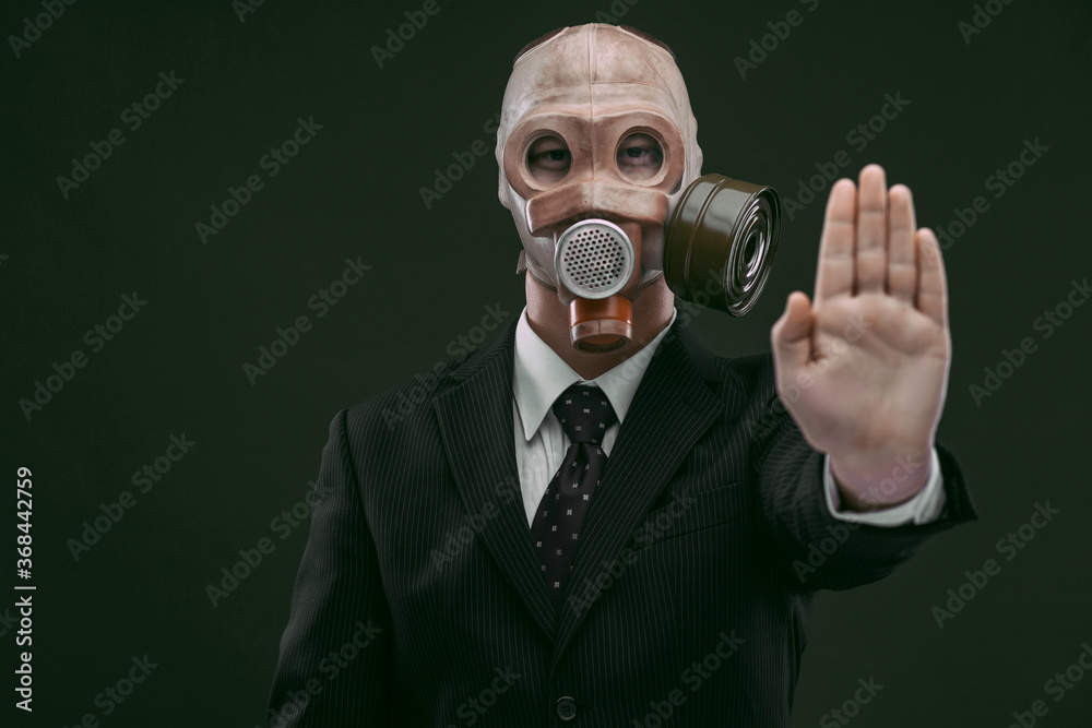 Portrait of a man wearing a business suit and an old gas mask showing his left palm, isolated on dark green background. Portrait of a man wearing a business suit and an old gas mask showing his left palm, isolated on dark green background.