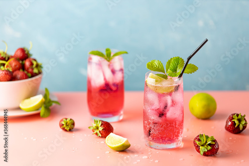 Two glasses with water drops of Strawberry mojito cocktail on light blue color background, pink board. Copy space, summer vacation and party concept