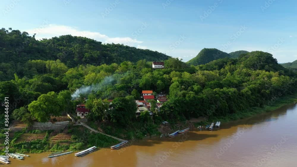 The houses surrounded by green vegetation along the Mekong river in Asia, Laos, Luang Prabang, in summer on a sunny day. The houses surrounded by green vegetation along the Mekong river in Asia, Laos, Luang Prabang, in summer on a sunny day.