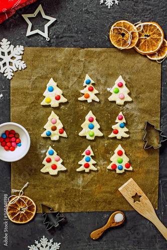 Christmas tree cookies with multicolored dough candies before baking on a sheet of parchment  close up