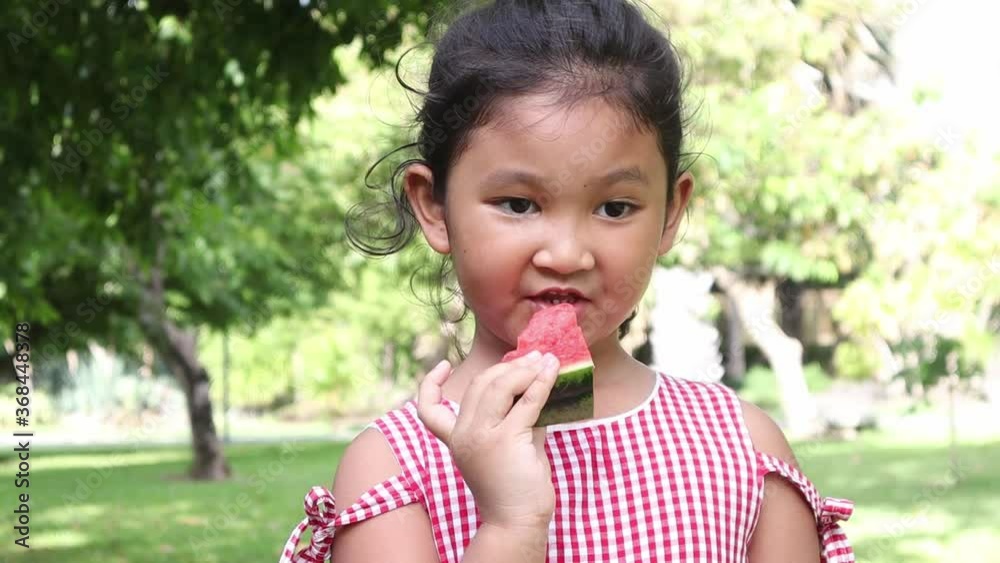 Happy child eating watermelon. Kid eat fruit outdoors. Little girl playing in the garden biting a slice of watermelon. Happy child eating watermelon. Kid eat fruit outdoors. Little girl playing in the garden biting a slice of watermelon.