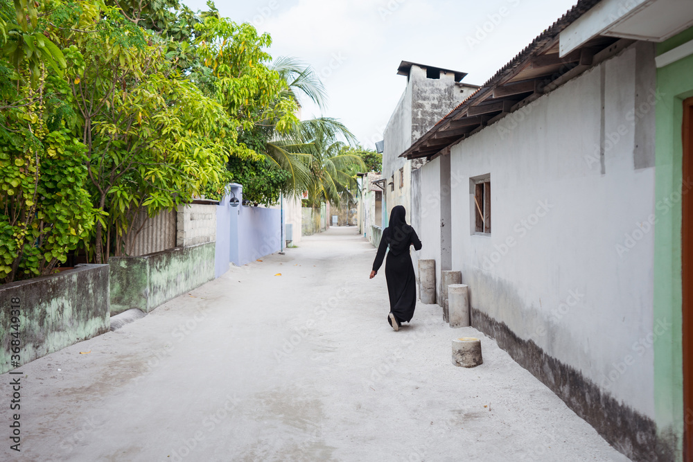 Unrecognizable Young Muslim woman in sand street in Bodufolhudhoo island village