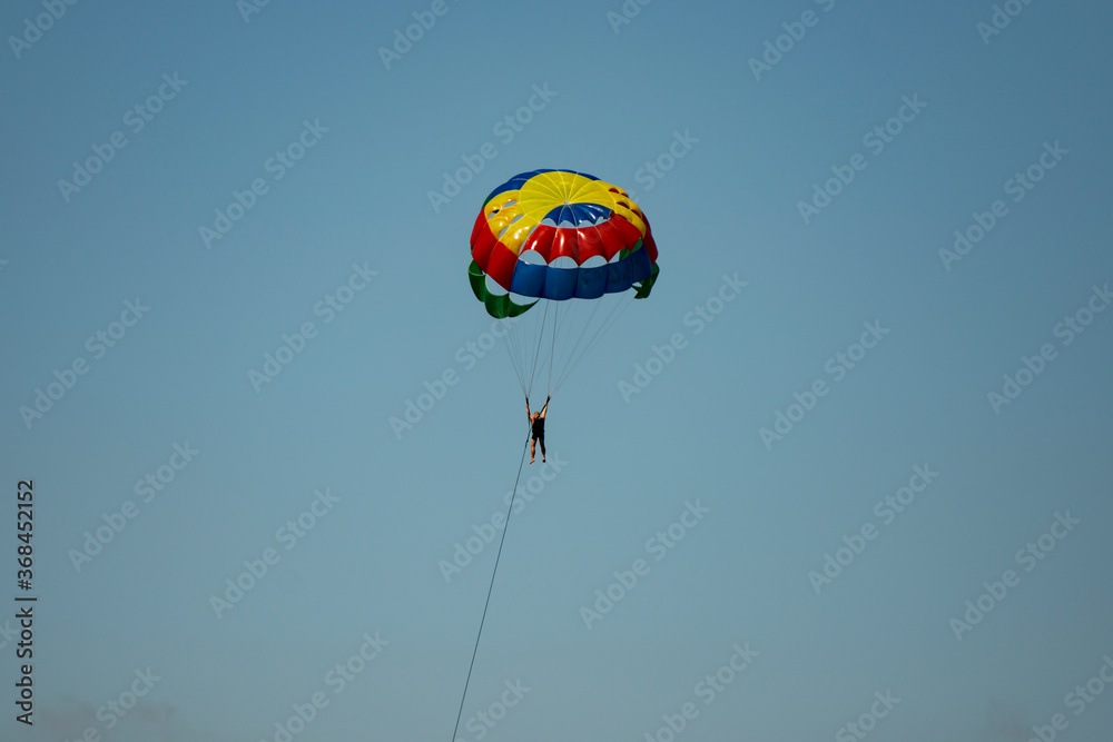 A man on a parachute parachuting over a blue lake. A man on a parachute parachuting over a blue lake.
