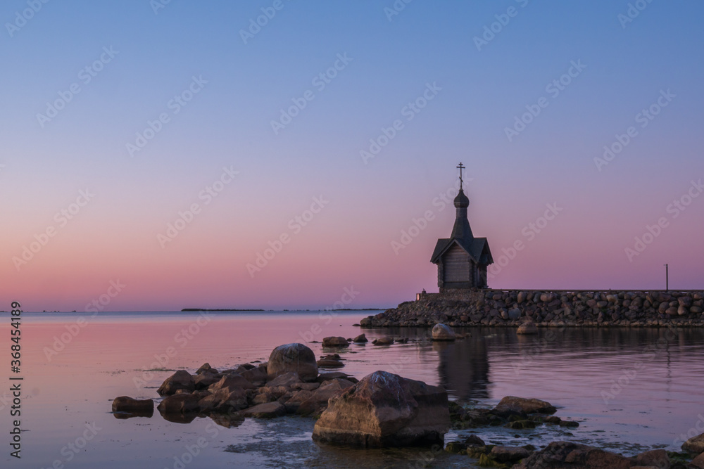 A church on the stone coast, against a beautiful blue sky. Big stones in the foreground and chapel in the background.