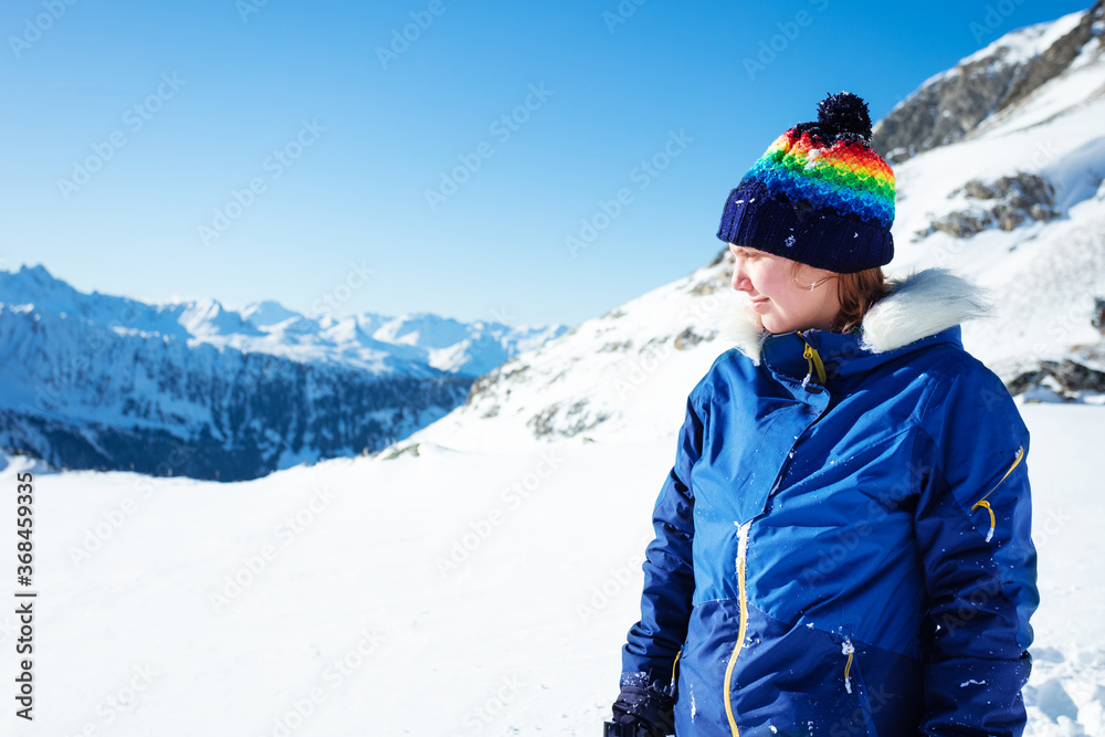 Portrait of girl in winter coat and hat walk high in the mountain on sunny day