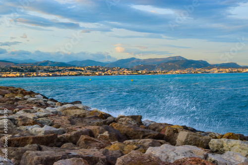 Waves crashing on the rocky breakwater against the backdrop of the Mediterranean sea and the Nice city background. France.