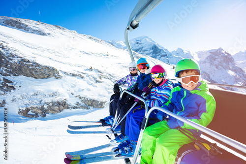 High portrait of four happy kids in vivid ski outfit lifting on chairlift on the mountain together and smiling