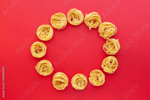 Tagliatelle raw pasta nests on red background, top view. Copy space